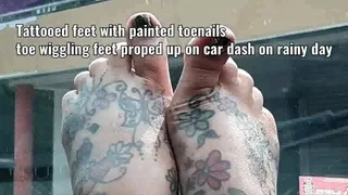 Tattooed feet with painted toenails toe wiggling feet proped up on car dash on rainy day mkv
