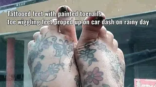 Tattooed feet with painted toenails toe wiggling feet proped up on car dash on rainy day