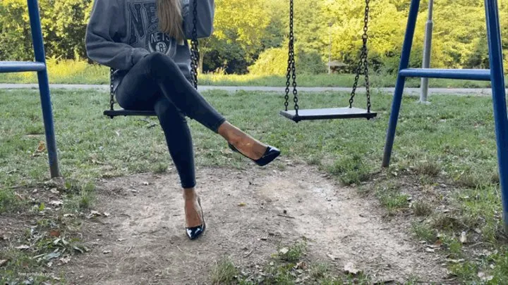 KIRA IS ON A PUBLIC PARK SWING IN HER HIGH HEELS