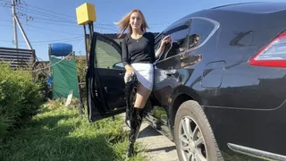 A girl in high-heeled boots poses, presses the pedals of a car, plays with boots