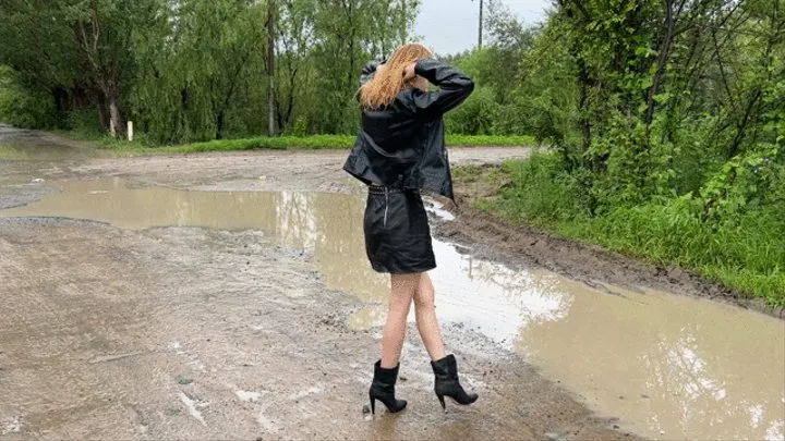 a girl in high-heeled leather boots walks through huge mud puddles in which her boots begin to sink