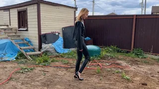 a girl in high-heeled shoes and in a latex suit walks through the mud, falls into it, wallows in the mud