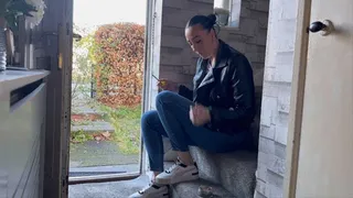 Smoking at the door in leather jacket, jeans and sneakers