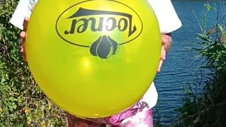 blowing big yellow balloon on nature