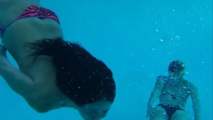 2 Gorgeous Women perform underwater acrobatics in the deep end.