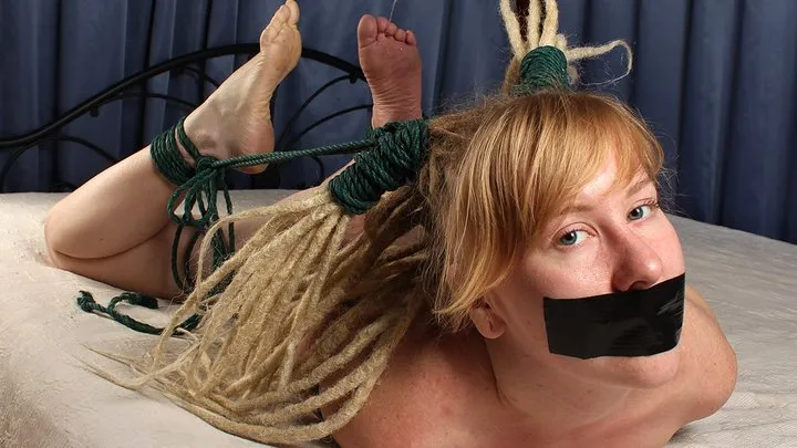 Florence: barefoot nude tapegagged girl wearing only a black corset hogtied on a bed with her feet tied with ropes to her hair, she is trying to move and gets tickled and teased by a camera man