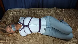 Tapegagged barefoot blonde Nancy in white shirt and light blue jeans, hogtied with violet hemp rope with her elbows tightly bound together, struggles on the bed