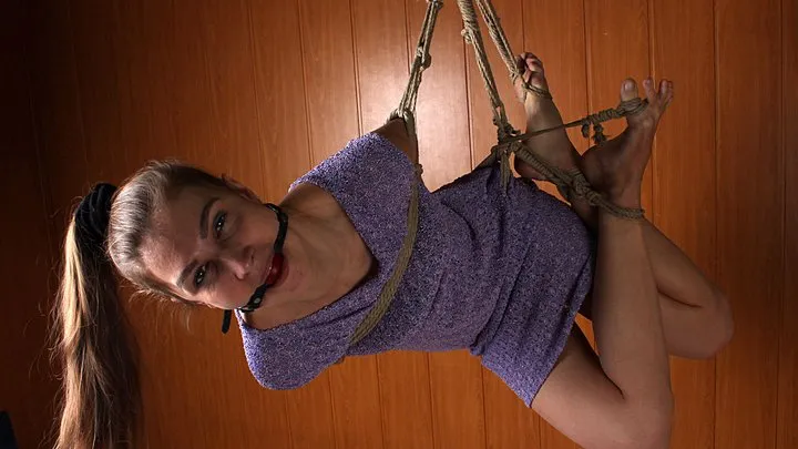 Ballgagged barefoot Sally in violet dress, suspended sideways with hemp rope, wiggles in the air