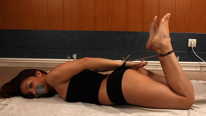 Tapegagged barefoot Aisha in black top and panties, hogtied with her hands and feet cuffed with black strict handcuffs, tied together with thin rope, rolls and wiggles on the floor