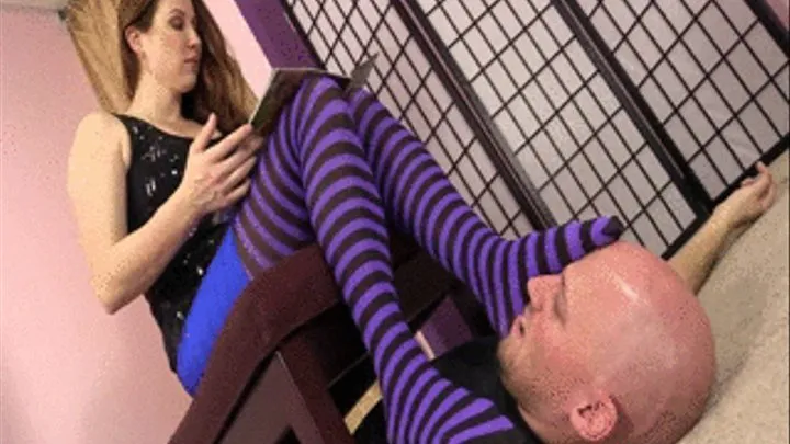 Mistress Shauna reads a book while playing with her slave's face using her stockings feet