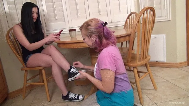 Mistress Cass sits at the table and orders her kneeling slave girl to get to work removing her shoes and suck on her sweaty black socks