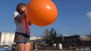 Titi blowing giant orange balloon outdoors