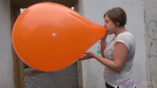 Simona inflates a giant orange balloon outside