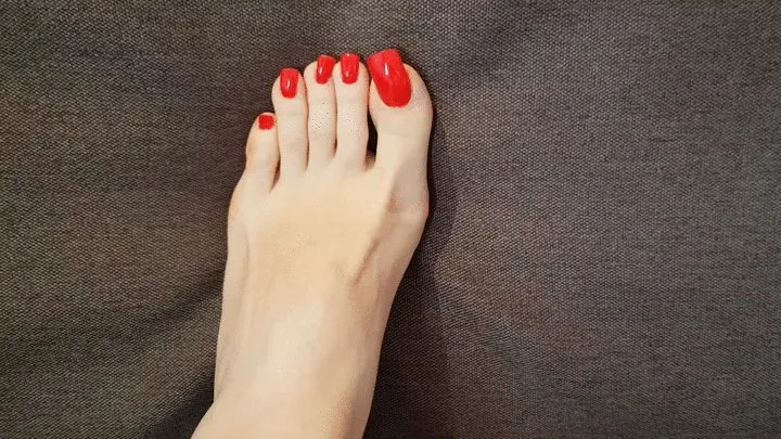 Toe pressing into couch with long red toenails