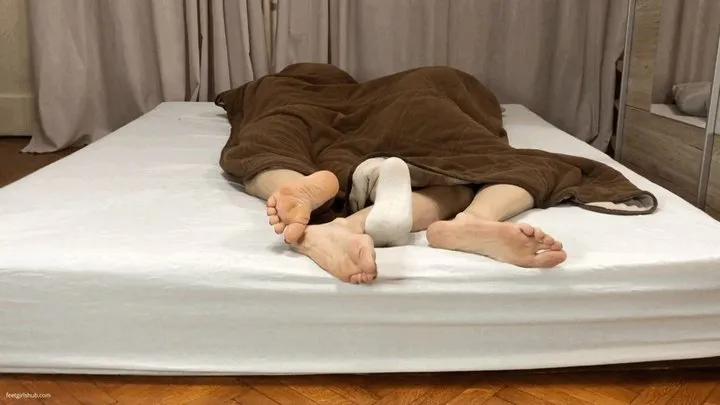 TWO GIRLS CUDDLING FEET UNDER BLANKET