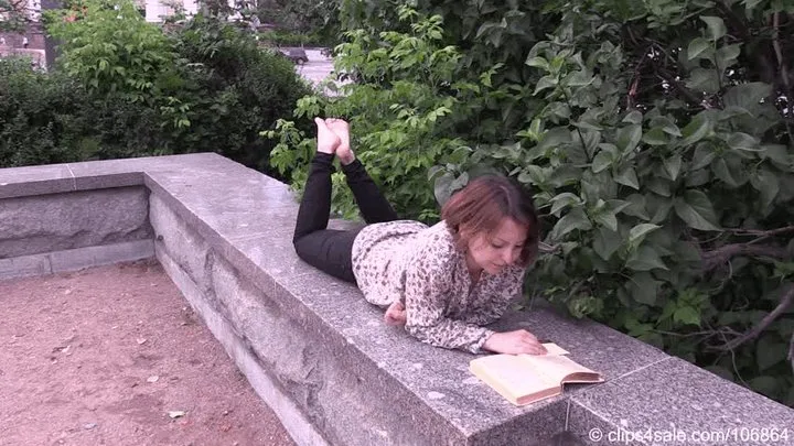 Barefoot Maria reads a book on the bench in the city square (Part 3 of 6)