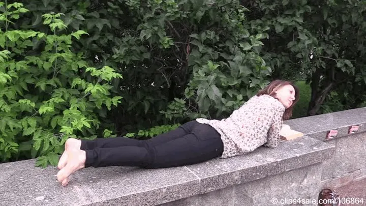 Barefoot Maria reads a book on the bench in the city square (Part 4 of 6)