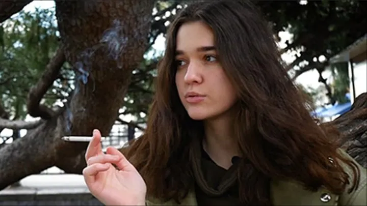 Young brunette is taking an unhurried stroll with allwhite 120mm cigarette