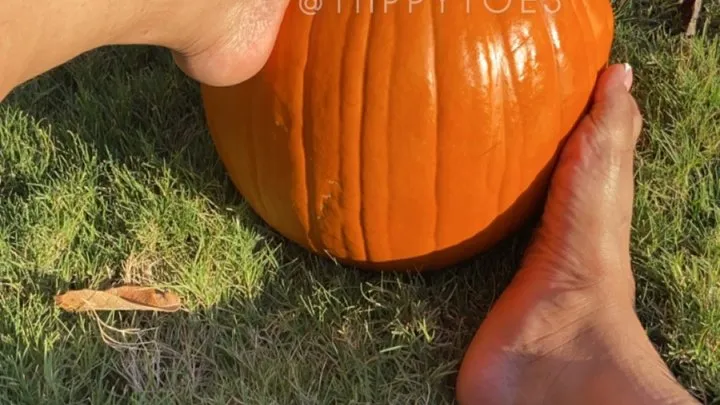 Tiippy is barefoot on the sidewalk stomping around and playing with a pumpkin with her feet